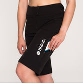 A person wearing a multicolored sports bra and black mountain bike shorts with the brand name 'Brava' visible on the shorts.